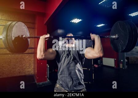 Uomo robusto e sportivo che solleva il peso pesante in camera oscura. Foto Stock