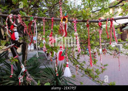 Braccialetti Martenitsa o Martisor rossi e bianchi, appesi sui rami dell'albero in fiore - tradizione primaverile bulgara e rumena Foto Stock