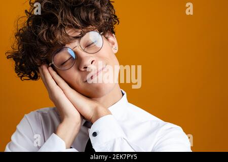 Studente maschile esausto in piedi indossando uniforme isolato su uno sfondo giallo, dormendo Foto Stock