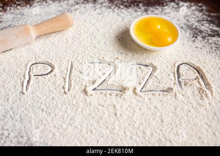 L'iscrizione Pizza su farina spruzzata, disegnata su fondo di legno, spilla e uova. Ricette di cottura. . Foto di alta qualità Foto Stock