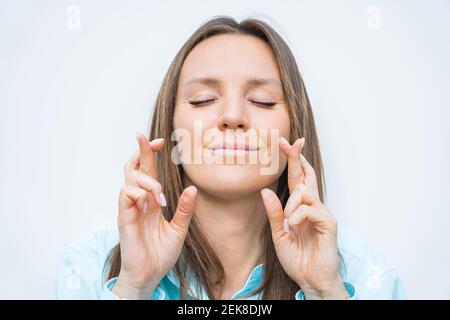 Giovane donna d'affari sorridente con gli occhi chiusi e incrociando le dita. Augurando Buona fortuna. Implorare il sogno diventa realtà, chiedendo meglio Foto Stock