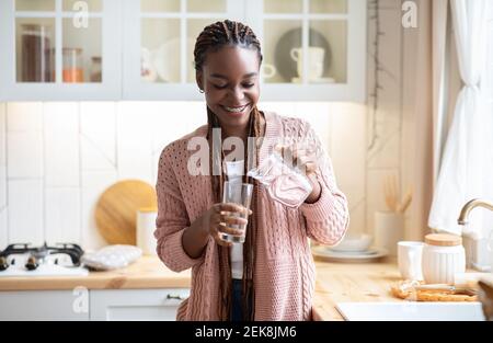 Donna nera assetata che beve acqua in cucina, versando liquido sano al vetro Foto Stock