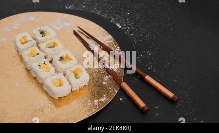 Consegna sushi. Panini dolci a base di riso, ananas, kiwi e mango. Rotola su sfondo oro e nero. Bastoncini di legno per sushi. Foto Stock