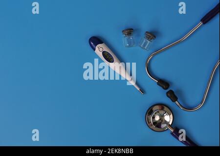 Disposizione dello stetoscopio, del termometro e delle fiale di vetro con spazio vuoto per il testo su sfondo blu Foto Stock