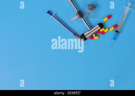 Layout di martello reflex, siringhe, flaconcini di vetro e pillole con spazio vuoto per il testo su sfondo blu Foto Stock
