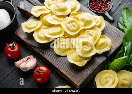 Ravioli crudi con ricotta e spinaci, su tagliere in legno, su fondo di tavola in legno nero Foto Stock