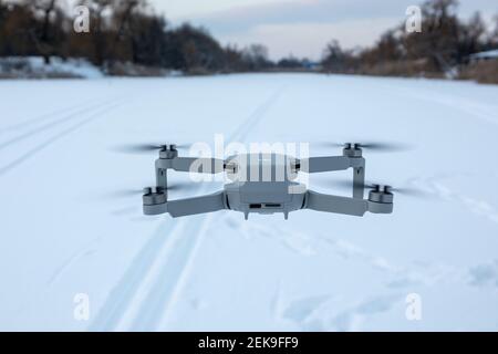 Kharkiv, Ucraina - 21 febbraio 2021: DJI Mavic Mini 2 drone volare in inverno paesaggio nevoso al tramonto. Nuovo hovering del dispositivo a quadcopia. Vista posteriore, fl Foto Stock