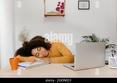 Donna stanca con un computer portatile che dorme sul tavolo di casa Foto Stock