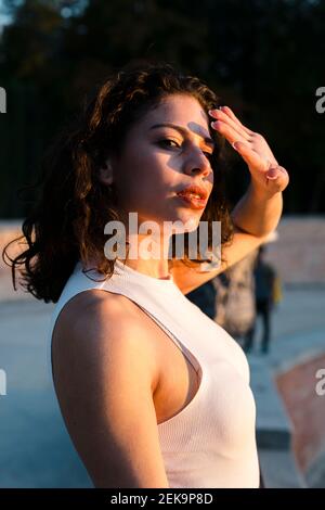 Donna giovane sicura che scherma gli occhi con la mano mentre si sta in piedi parcheggia al tramonto Foto Stock