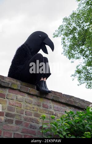 Donna in costume da corvo seduta su un muro di ritegno contro il cielo Foto Stock
