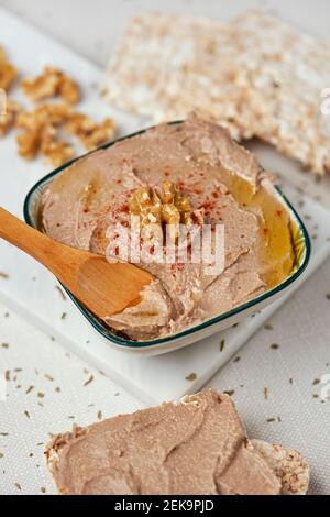 una ciotola rettangolare in ceramica con un hummus appetitoso, fatta con ceci, noce e rosmarino, su un tavolo, accanto ad alcune torte di riso soffiato Foto Stock