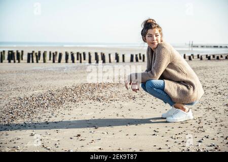 Bella donna con posizione squatting guardando via alla spiaggia su giorno di sole Foto Stock