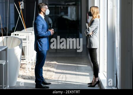 Uomini d'affari che indossano la maschera protettiva in piedi a distanza sociale Durante il lavoro in ufficio durante il COVID-19 Foto Stock