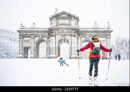 Uomo e donna sciano sulla neve contro la porta di Alcala durante la Storm Filomena nel 2021 a Madrid, Spagna Foto Stock