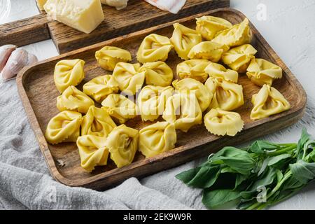 Tortellini italiani fatti in casa con ingredienti, prosciutto, basilico, pesto, mozzarella, su vassoio di legno Foto Stock