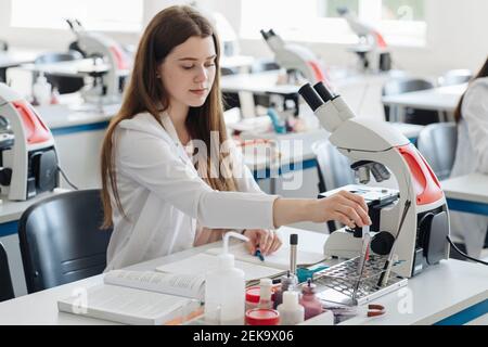 Giovane ricercatrice femminile in camice bianco che lavora in laboratorio con un campione di laboratorio Foto Stock
