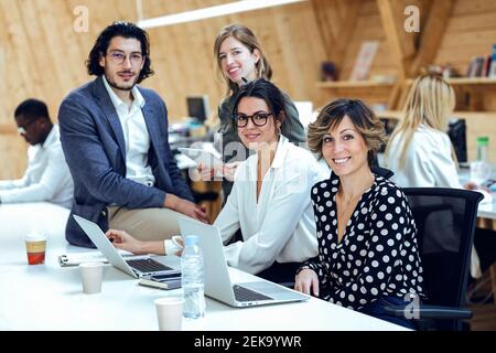 Un team di lavoro sorridente con un notebook che fa idee creative alla scrivania in un posto di lavoro Foto Stock