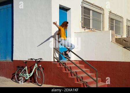 Giovane donna scivolante su ringhiera da struttura costruita bianca durante giorno di sole Foto Stock