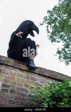 Donna aggressiva in costume corvo seduta su muro di ritegno contro cielo Foto Stock