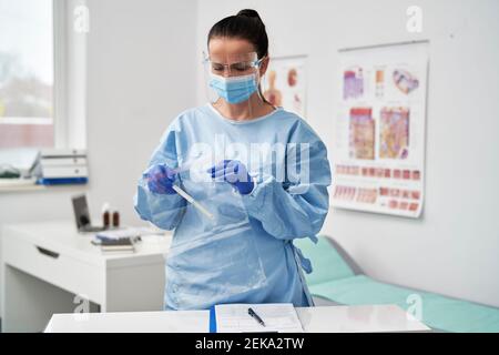 Medico femminile maturo con visiera protettiva che mette il campione medico in un sacchetto con cerniera Foto Stock