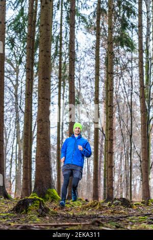 Uomo che fa jogging sul sentiero tra alberi di conifere nella foresta Foto Stock