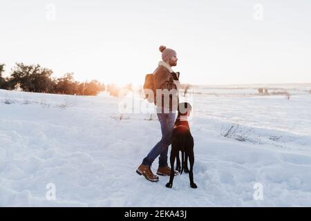 Zaino in spalla maschile in piedi con il cane Great Dane mentre si guarda via nella neve Foto Stock