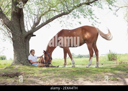 Donna che si rilassa in un campo con un cavallo in piedi vicino lei Foto Stock