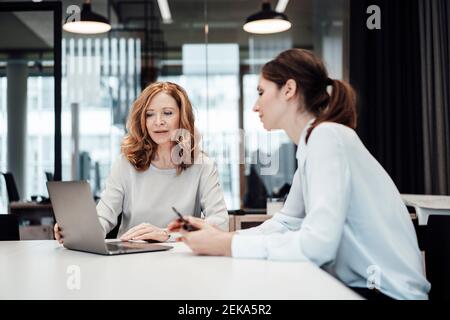 Donne professionisti che discutono sopra il laptop in sala illuminata della scheda a. ufficio Foto Stock