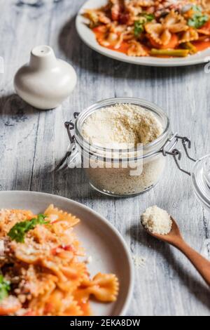Due piatti di pasta vegana con verdure e vasetto di Parmigiano grattugiato di vegano Foto Stock
