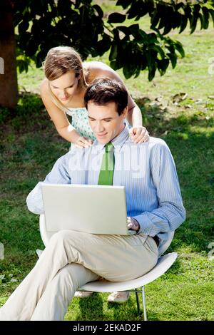 Uomo d'affari che usa un computer portatile e una donna che guarda da dietro Foto Stock