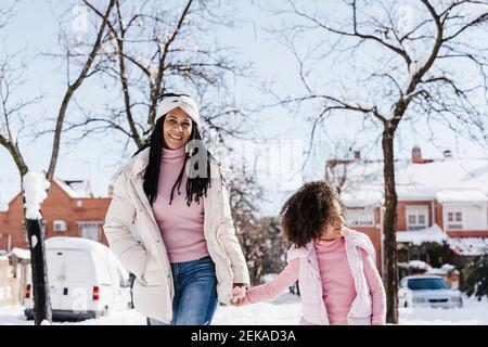 Madre e figlia che tengono le mani mentre camminano sulla strada durante inverno Foto Stock