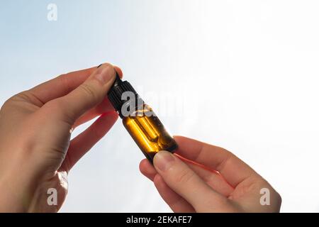 Bottiglia di olio cbd o thd in mano umana, sparato contro il cielo blu. Olio essenziale, prodotti naturali per la salute, integratori calmanti Foto Stock