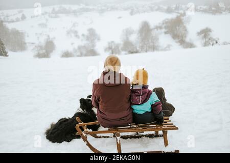 Madre e bambini con Border Collie seduto sulla neve coperta campo contro la montagna Foto Stock