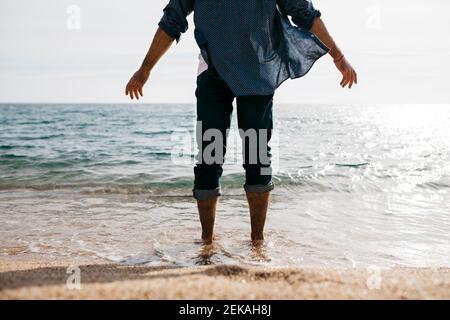 Uomo maturo in piedi nel bordo dell'acqua contro il cielo chiaro a. spiaggia
