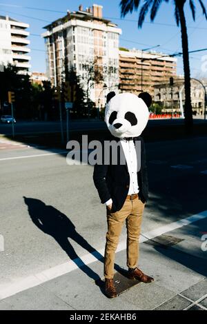 Uomo d'affari che indossa maschera di panda in piedi con le mani in tasche a. città Foto Stock