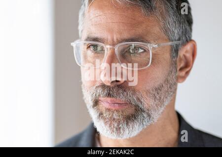Primo piano di un uomo d'affari maturo che indossa occhiali che guardano via mentre si sta in piedi a casa Foto Stock