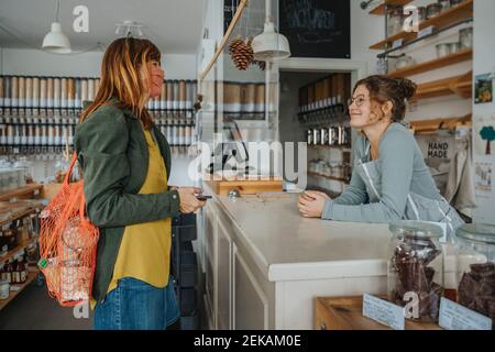 Cliente femminile che parla con l'impiegato in un negozio di rifiuti zero durante pandemia Foto Stock