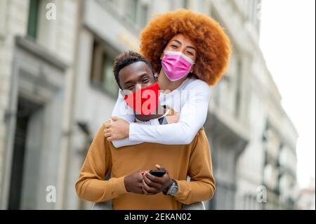 Donna che indossa maschera piggybacking sull'uomo in città Foto Stock