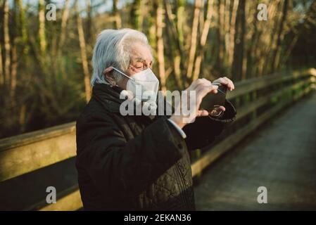 Donna anziana che fotografa tramite smartphone sul ponte pedonale durante il COVID-19 Foto Stock