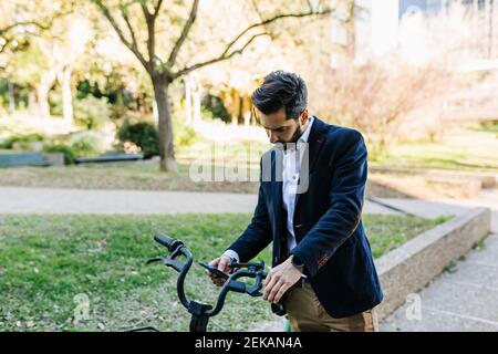 Uomo d'affari che usa il telefono cellulare mentre si è in piedi in bicicletta al parcheggio Foto Stock