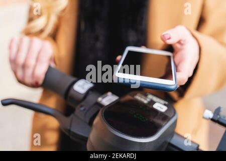 Donna che usa lo smartphone per sbloccare lo scooter elettrico a spinta Foto Stock