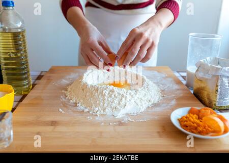 Donna che aggiunge l'uovo nella farina in cucina a casa Foto Stock