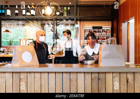 Uomo e donna proprietario con chef che parla mentre si prepara prendere Fuori cibo al bar durante COVID-19 Foto Stock