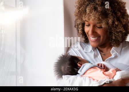 Donna sorridente che tiene il neonato mentre si trova a casa Foto Stock