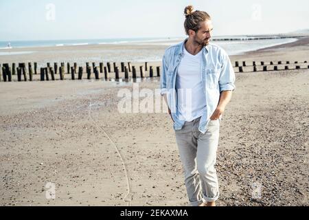 Bell'uomo giovane con le mani in tasca guardando via mentre passeggiate sulla spiaggia Foto Stock