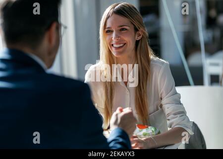 Donna d'affari sorridente che pranza con un collega mentre si siede in caffetteria in ufficio Foto Stock