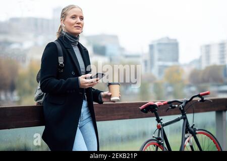 Donna che tiene il telefono cellulare mentre ascolta la musica attraverso le cuffie bicicletta Foto Stock