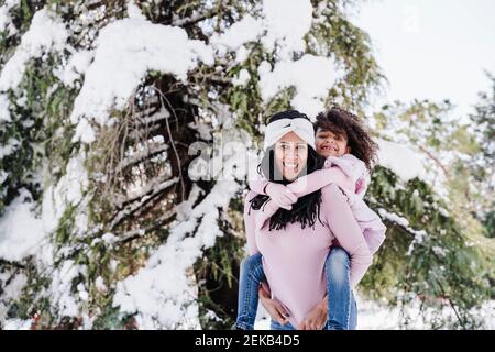 Madre sorridente che fa un giro in piggyback alla figlia nel parco Foto Stock