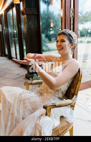 Felice sposa che si aggrappano le mani mentre si siede sulla sedia al banchetto Foto Stock