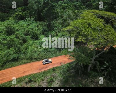 Costa d'Avorio, Korhogo, vista aerea di un'auto 4x4 che guida lungo la strada sterrata tagliando attraverso la giungla verde Foto Stock